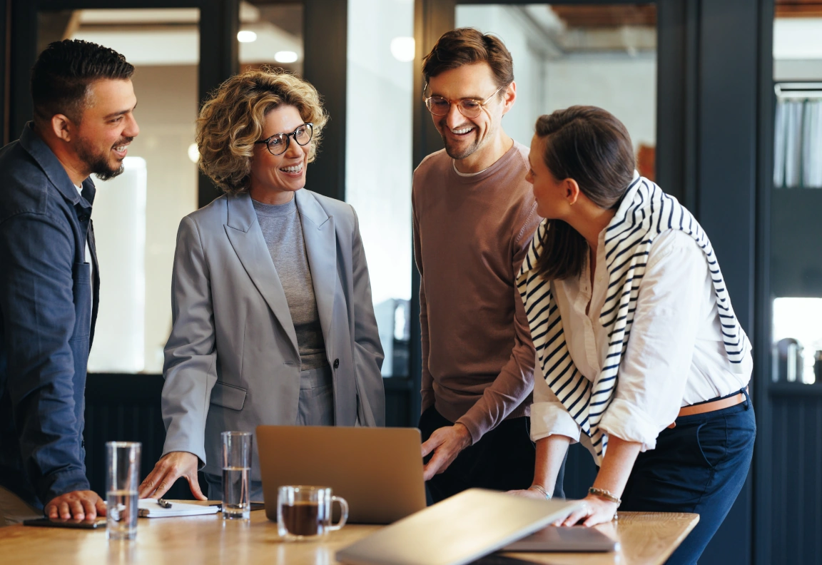 People standing behind a conference table looking at a laptop.