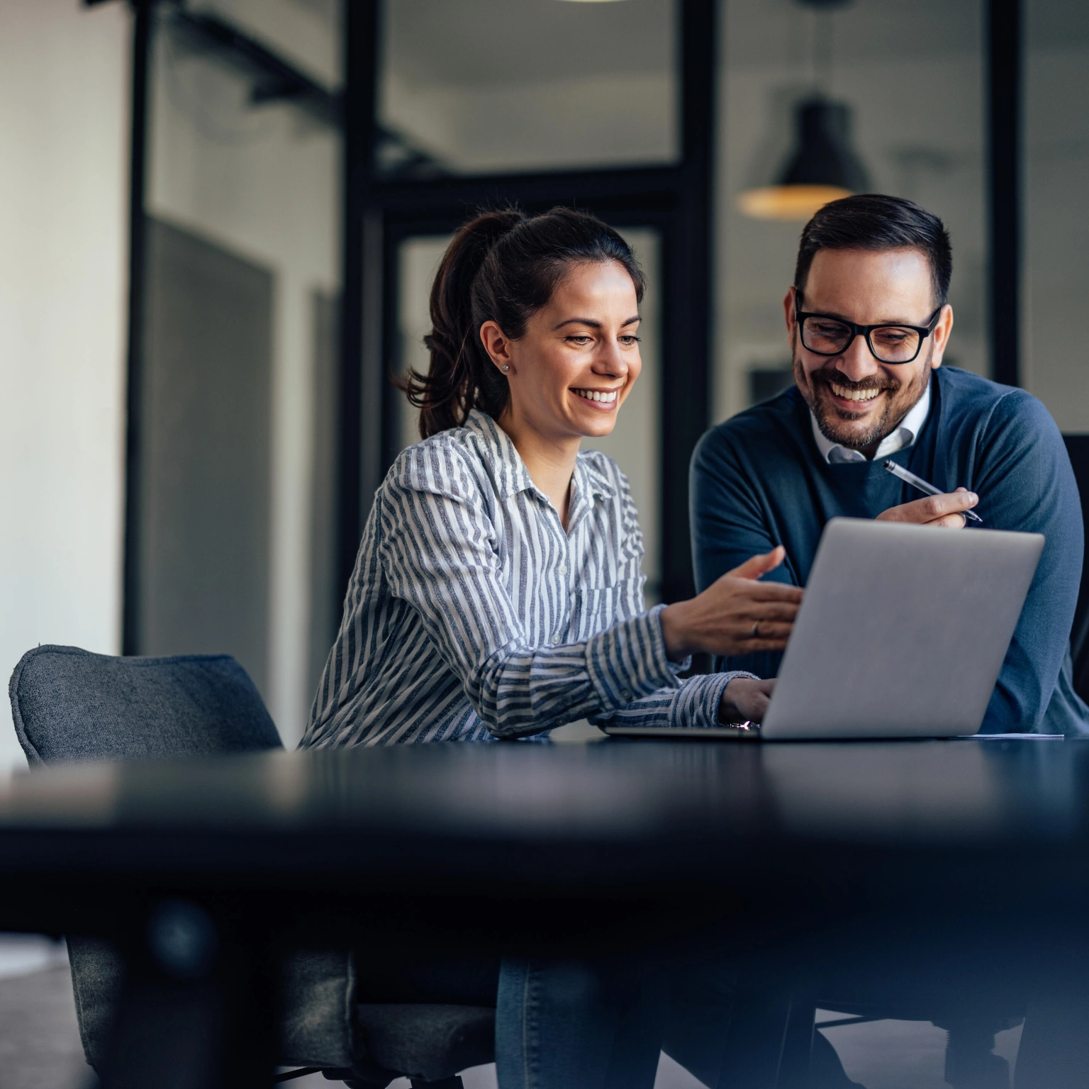 Smiling man and woman collaborating behind a laptop.