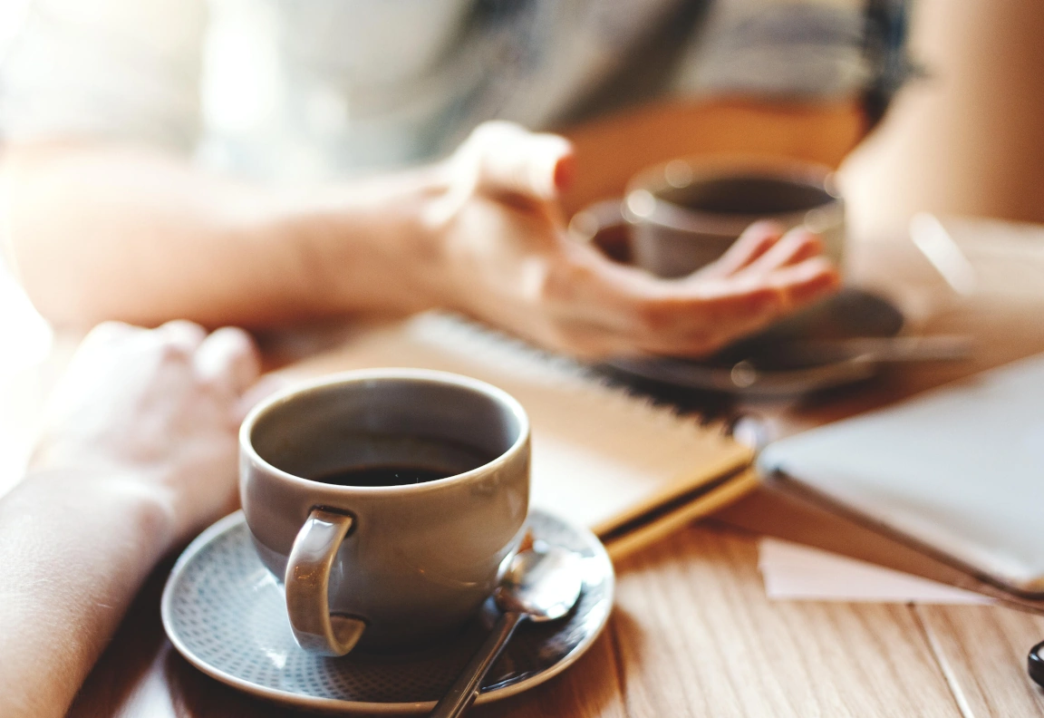 Two cups of coffee on a table surrounded by papers and a notebook.