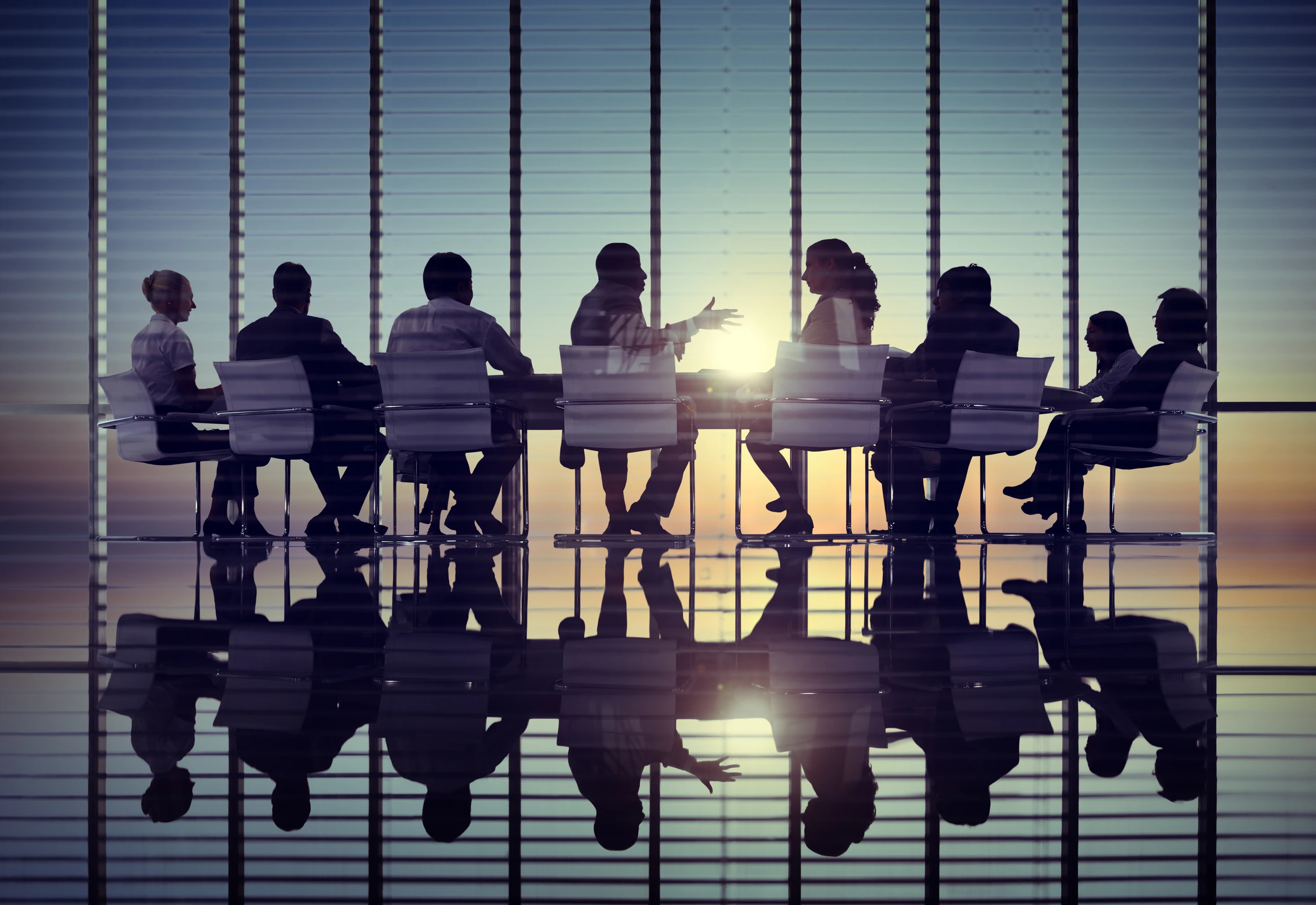 Team sitting at a table in a large reflective meeting room.
