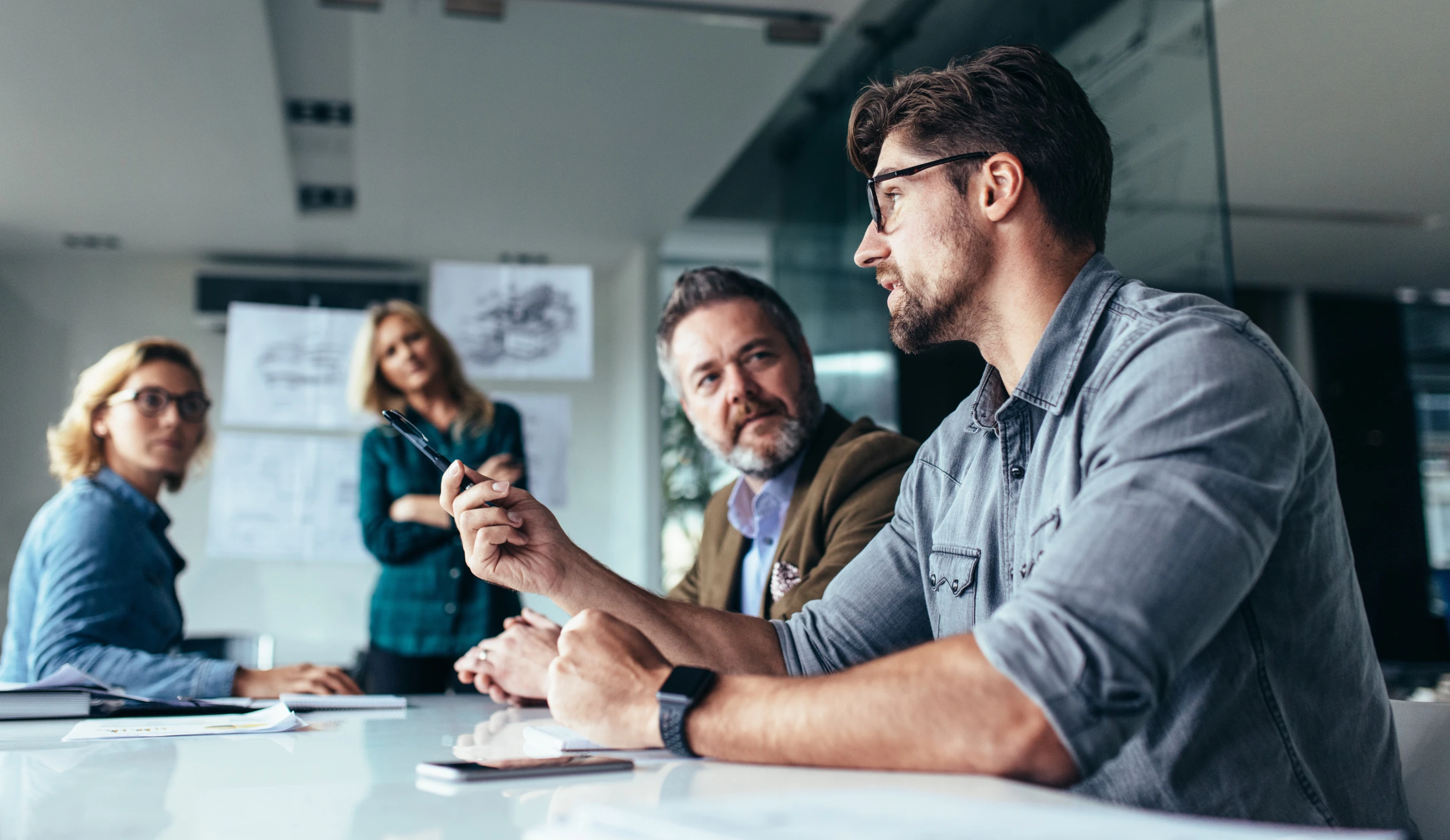 Team in a meeting at a table, one man is speaking while three others listen attentively.